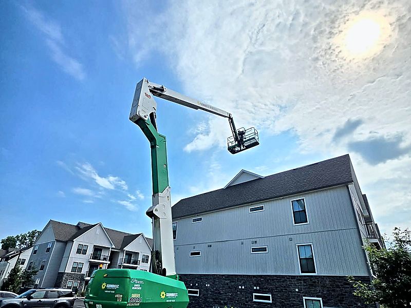 Articulating boom lift extended to the third-story roofline of a multi-family building during roofing and exterior restoration
