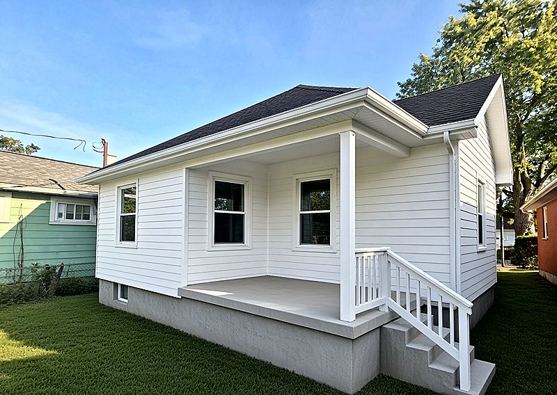 Restored residential house exterior with new white lap siding, charcoal shingle roof, windows, and rebuilt front porch